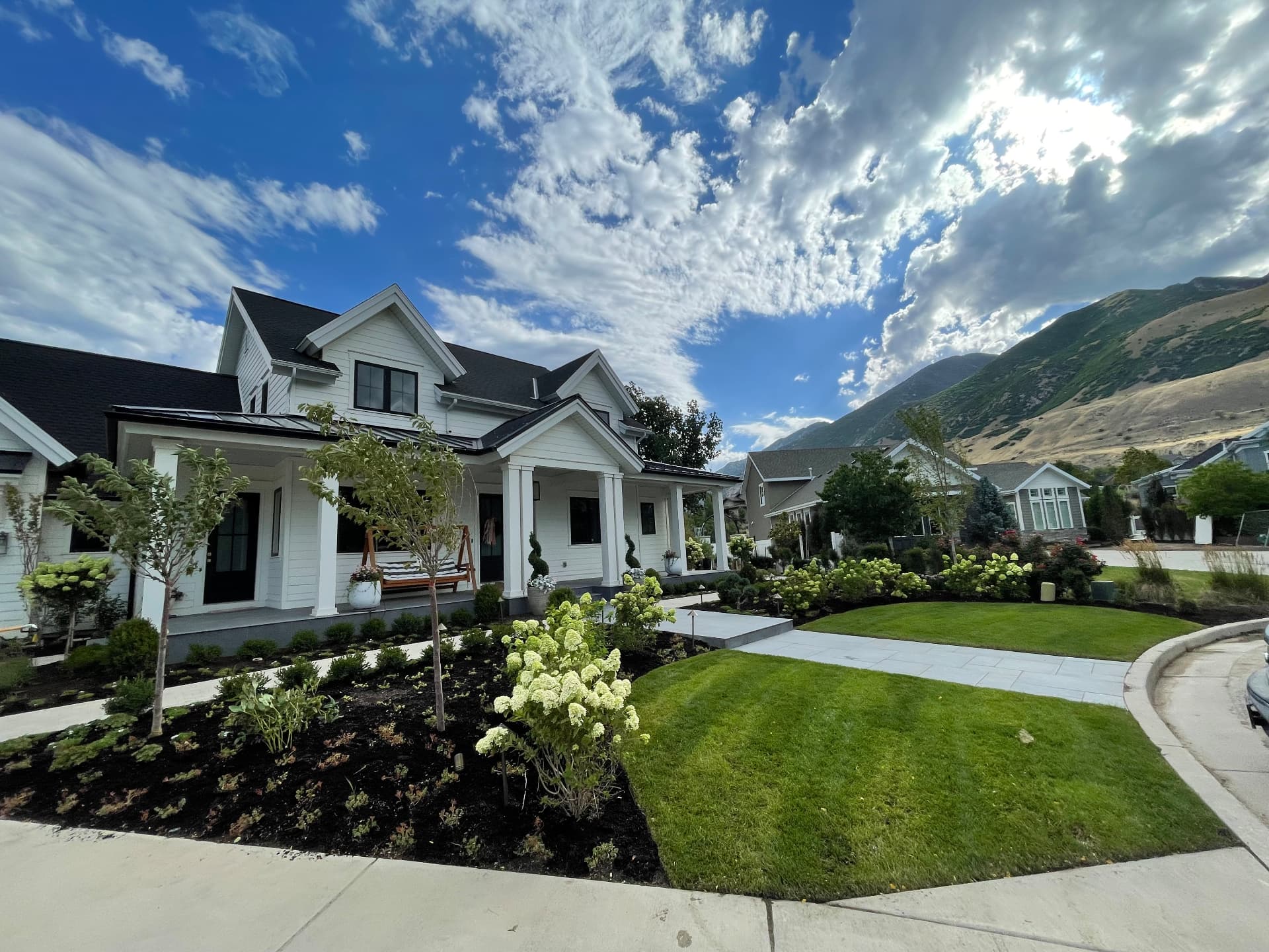Front yard with a manicured lawn, planted beds and a concrete walkway leading to a white home, mountains behind
