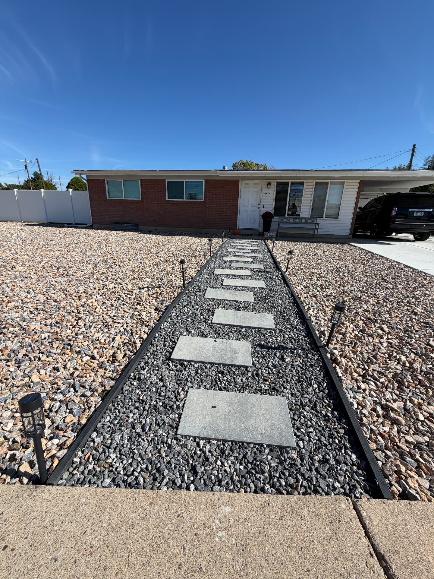 Front yard rock xeriscape with a black-gravel path of concrete stepping stones lined with solar lights