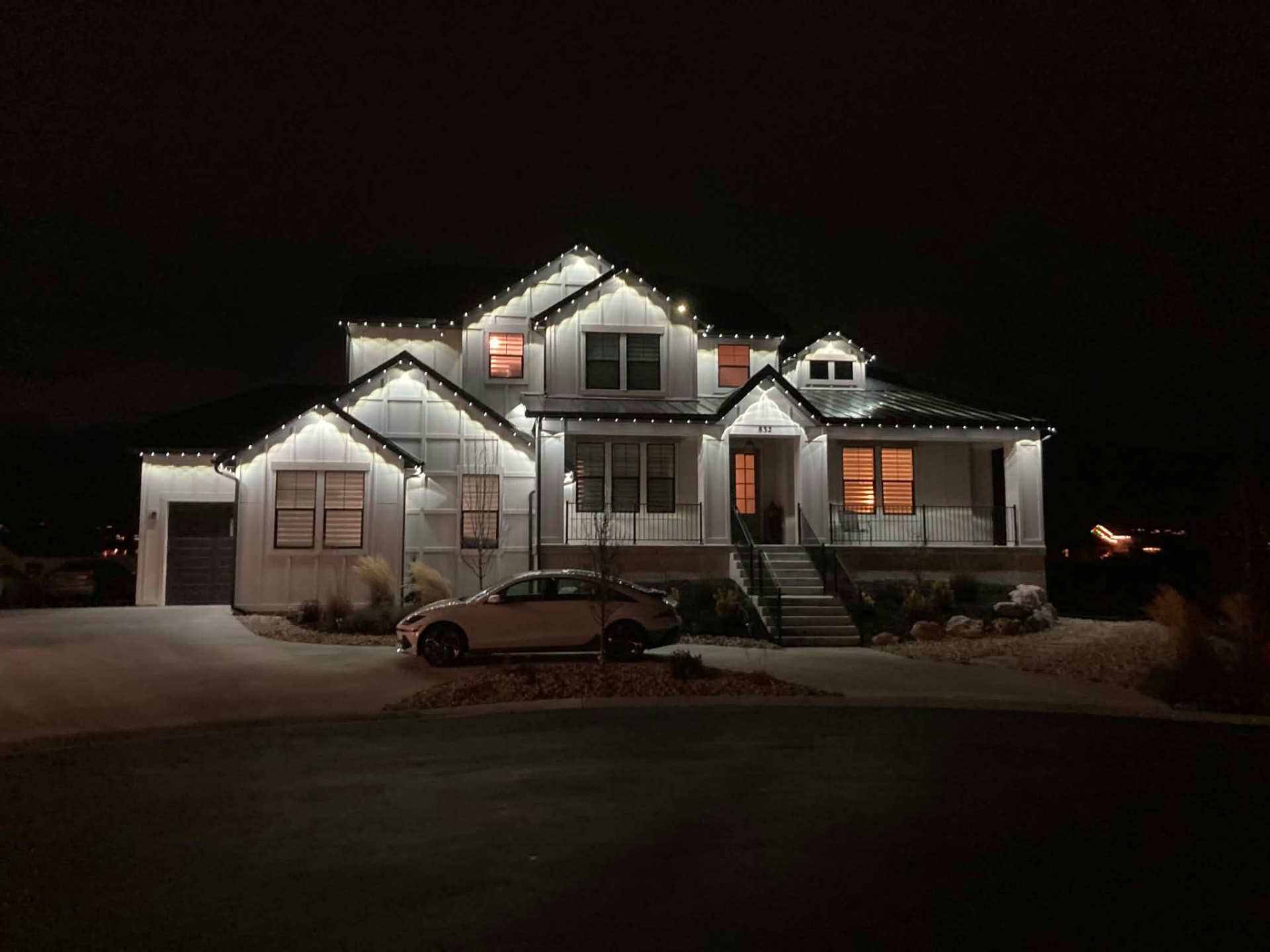 White two-story home at night with warm-white permanent lighting outlining the gables and eaves